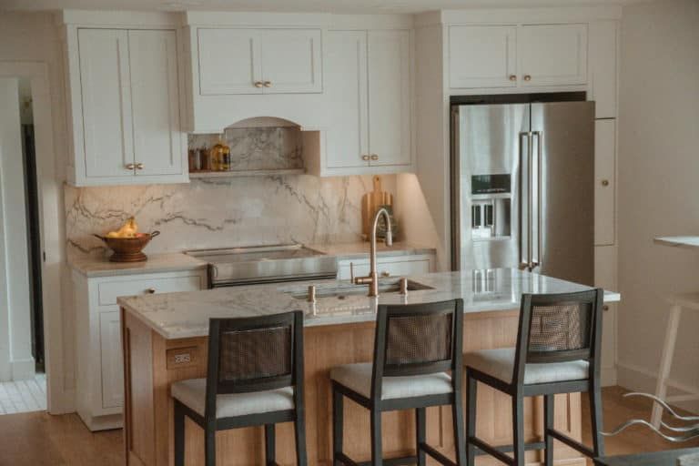 A kitchen with white cabinets , a stainless steel refrigerator , a sink , and a stove.