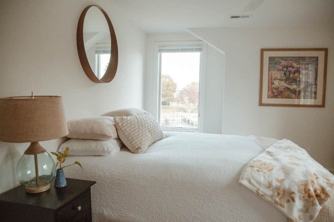 A bedroom with a bed , nightstand , lamp and mirror.