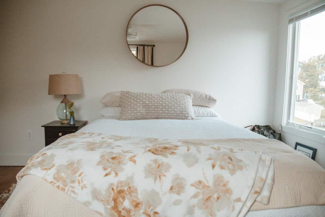 A bedroom with a bed , nightstand , lamp and mirror.