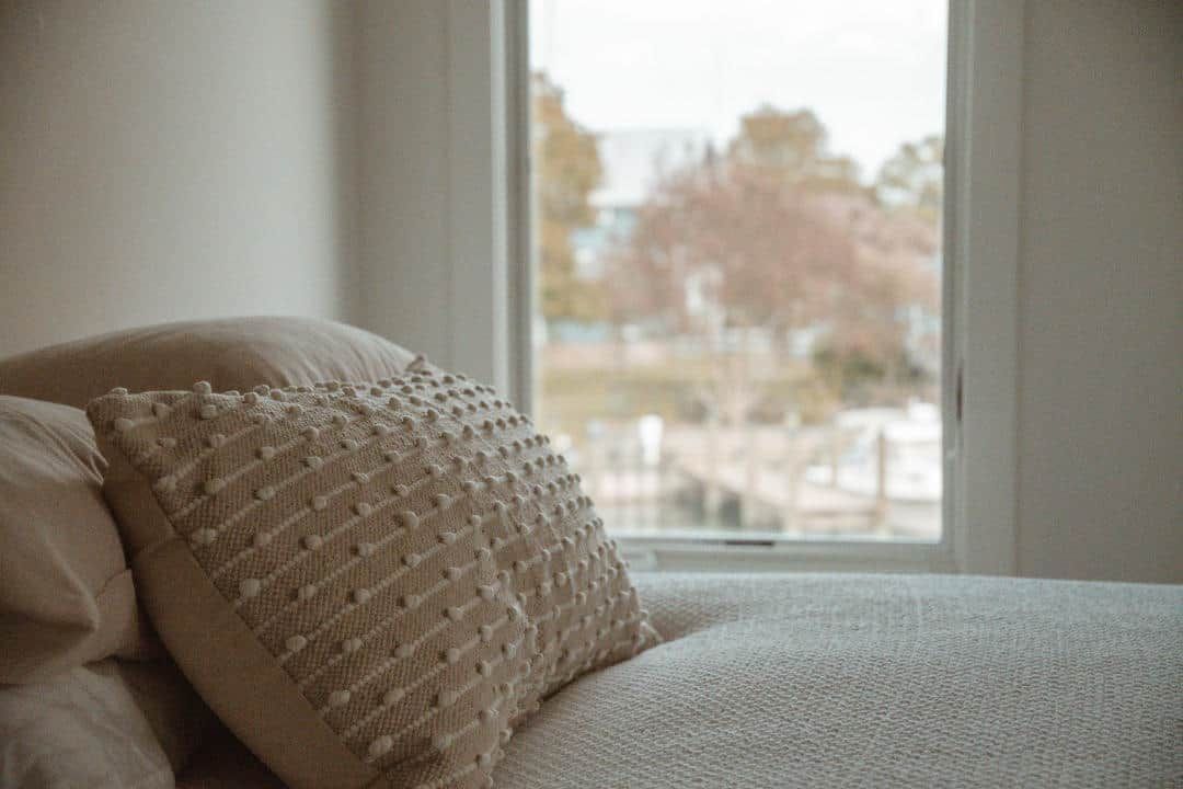 A bed with a pillow on it and a window in the background.