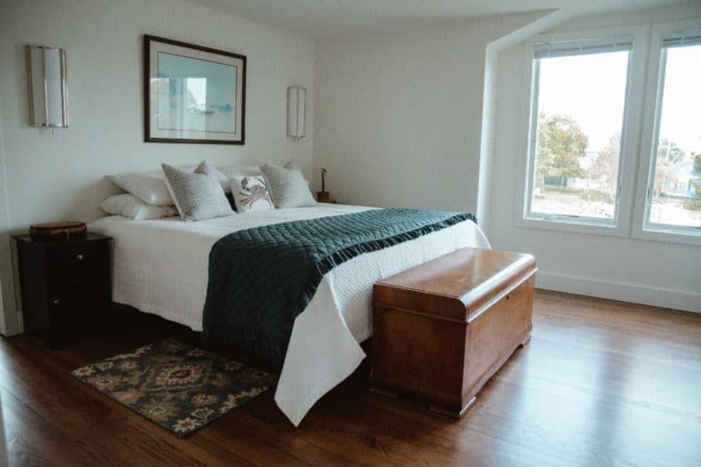 A bedroom with a bed , a bench , and two windows.