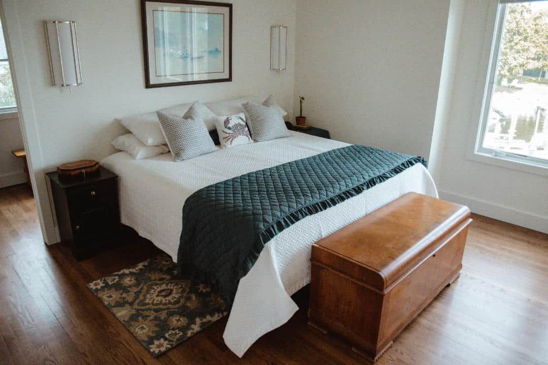 A bedroom with a bed , nightstand , trunk and window.