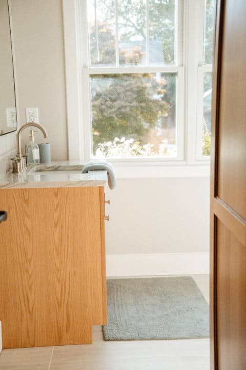 A bathroom with a sink , mirror and window.
