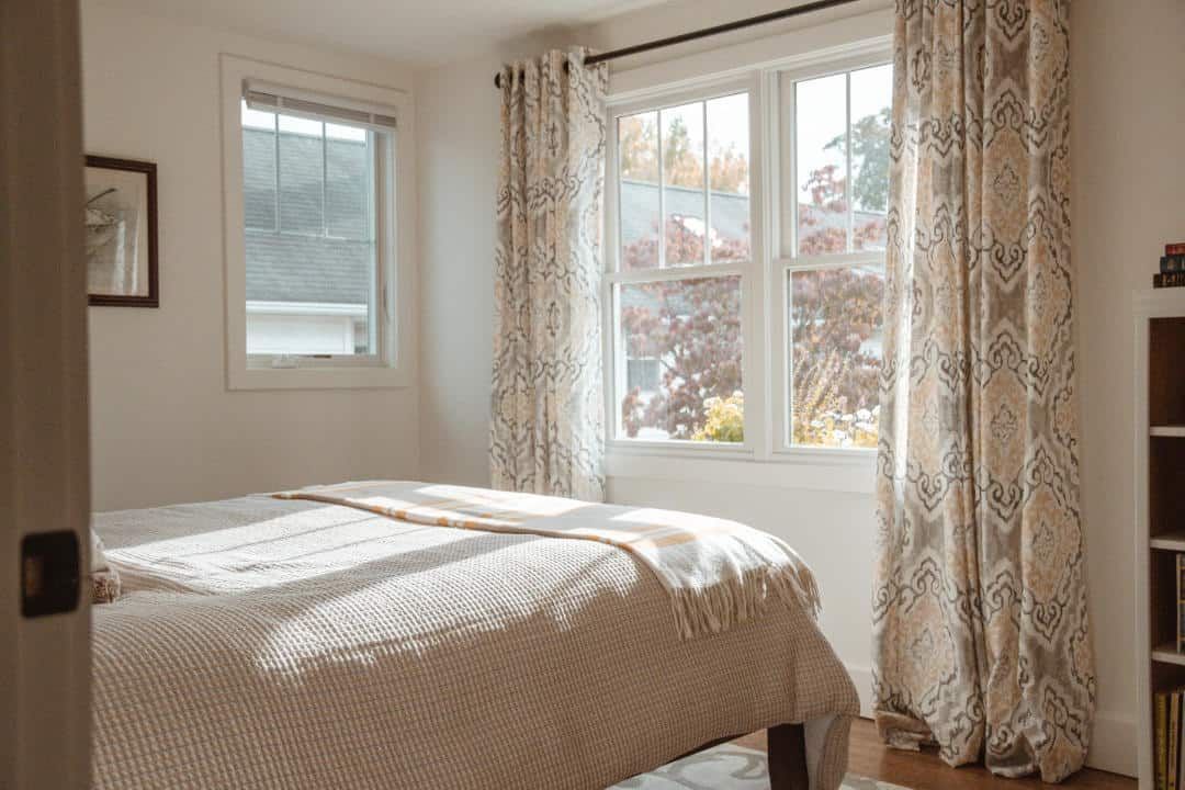 A bedroom with a bed , window , curtains and a bookshelf.
