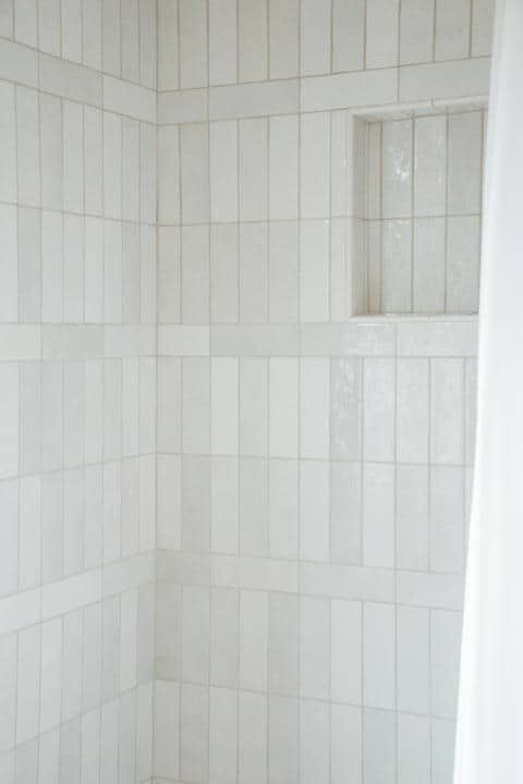 A bathroom with white tiles and a shower curtain.