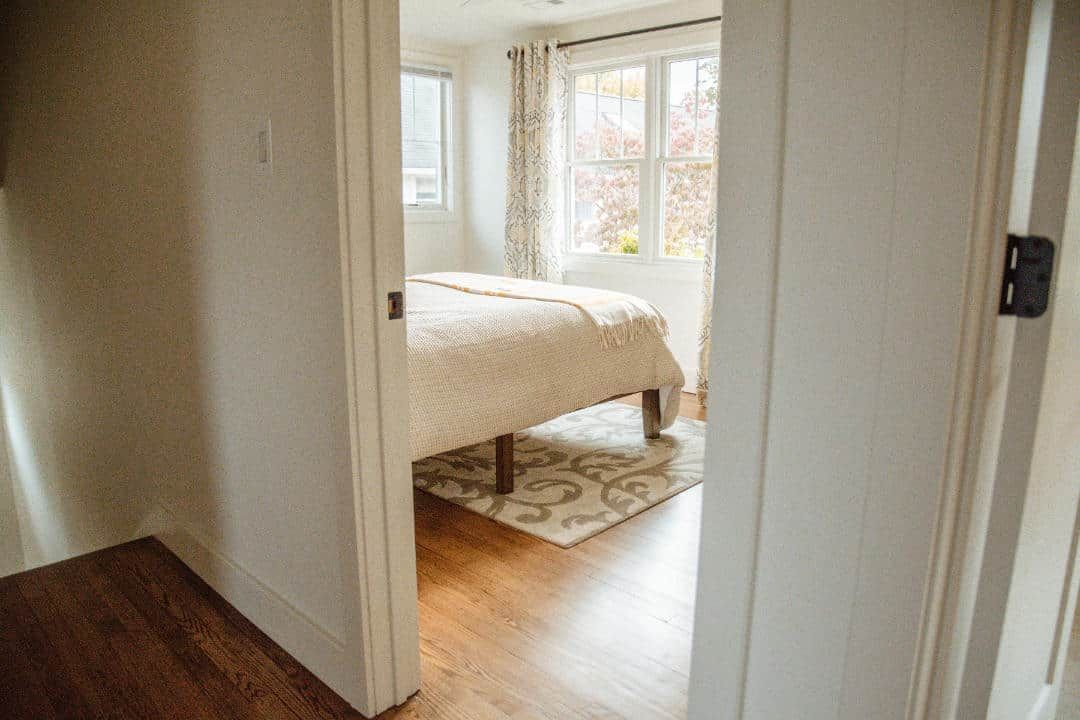 A hallway leading to a bedroom with a bed and a window.
