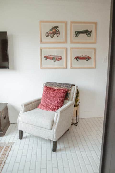 A chair with a red pillow is sitting in a living room next to a wall with pictures of cars on it.