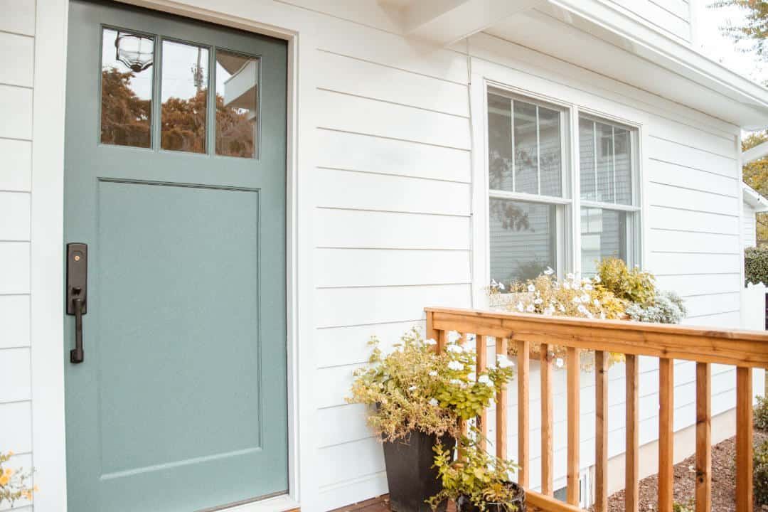 A white house with a blue door and a wooden deck.