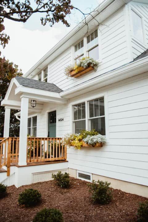 A white house with a porch and flowers in the windows