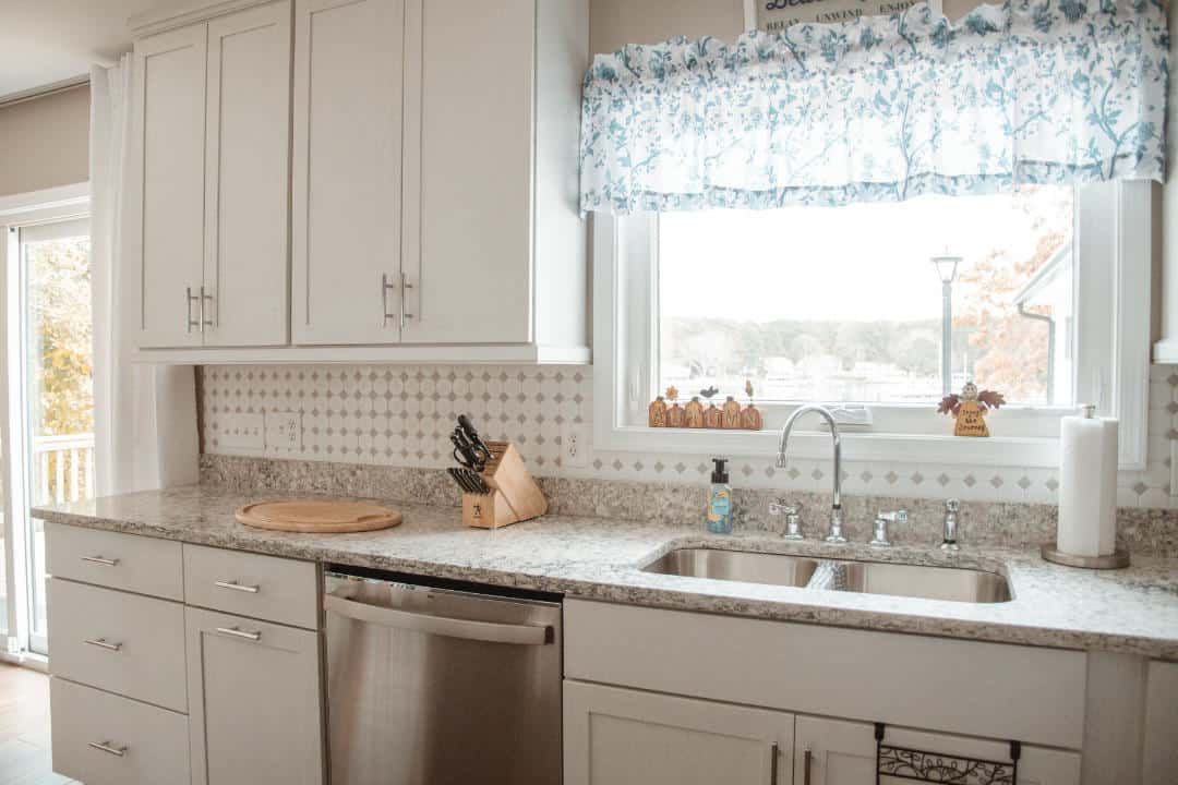 A kitchen with white cabinets , stainless steel appliances , a sink and a window.