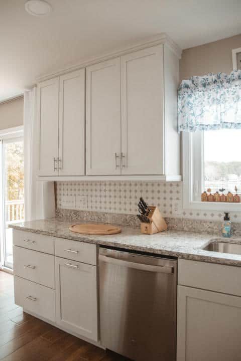 A kitchen with white cabinets , stainless steel appliances , a sink , and a window.