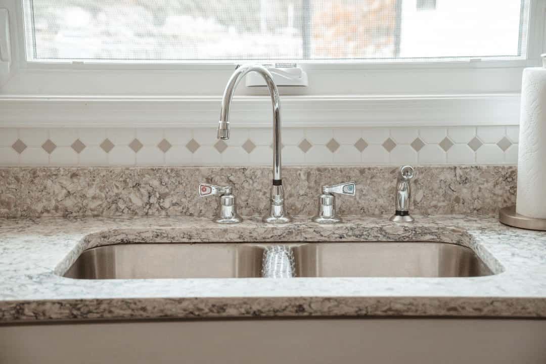 A kitchen sink with a faucet and a window in the background.