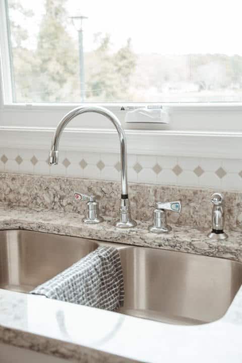 A kitchen sink with a faucet and a window in the background.