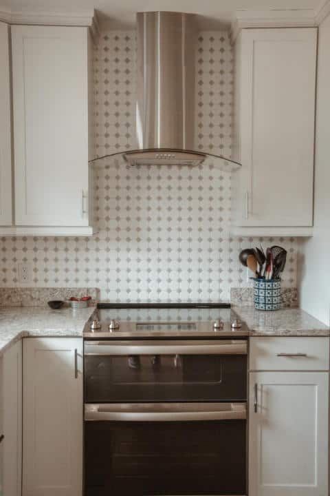 A kitchen with white cabinets , a stove , and a hood.