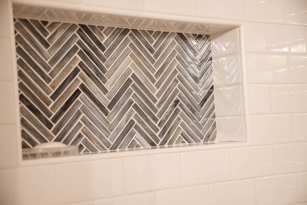 A shower niche with a herringbone tile pattern in a bathroom.
