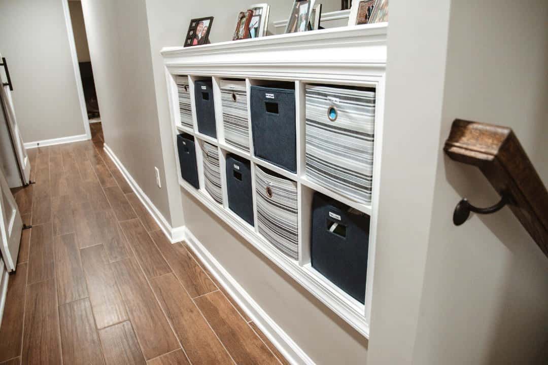 A hallway with a staircase and a shelf with baskets on it.