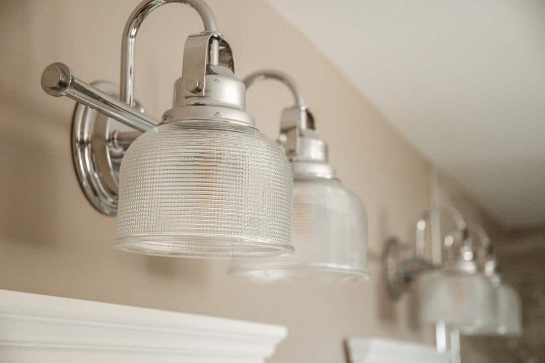 A bathroom vanity light with clear glass shades is hanging on a wall.