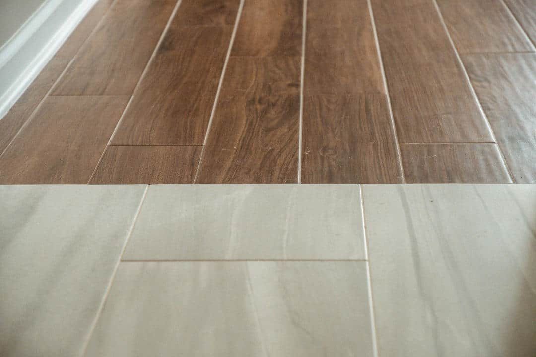 A close up of a wooden floor next to a white tile floor.