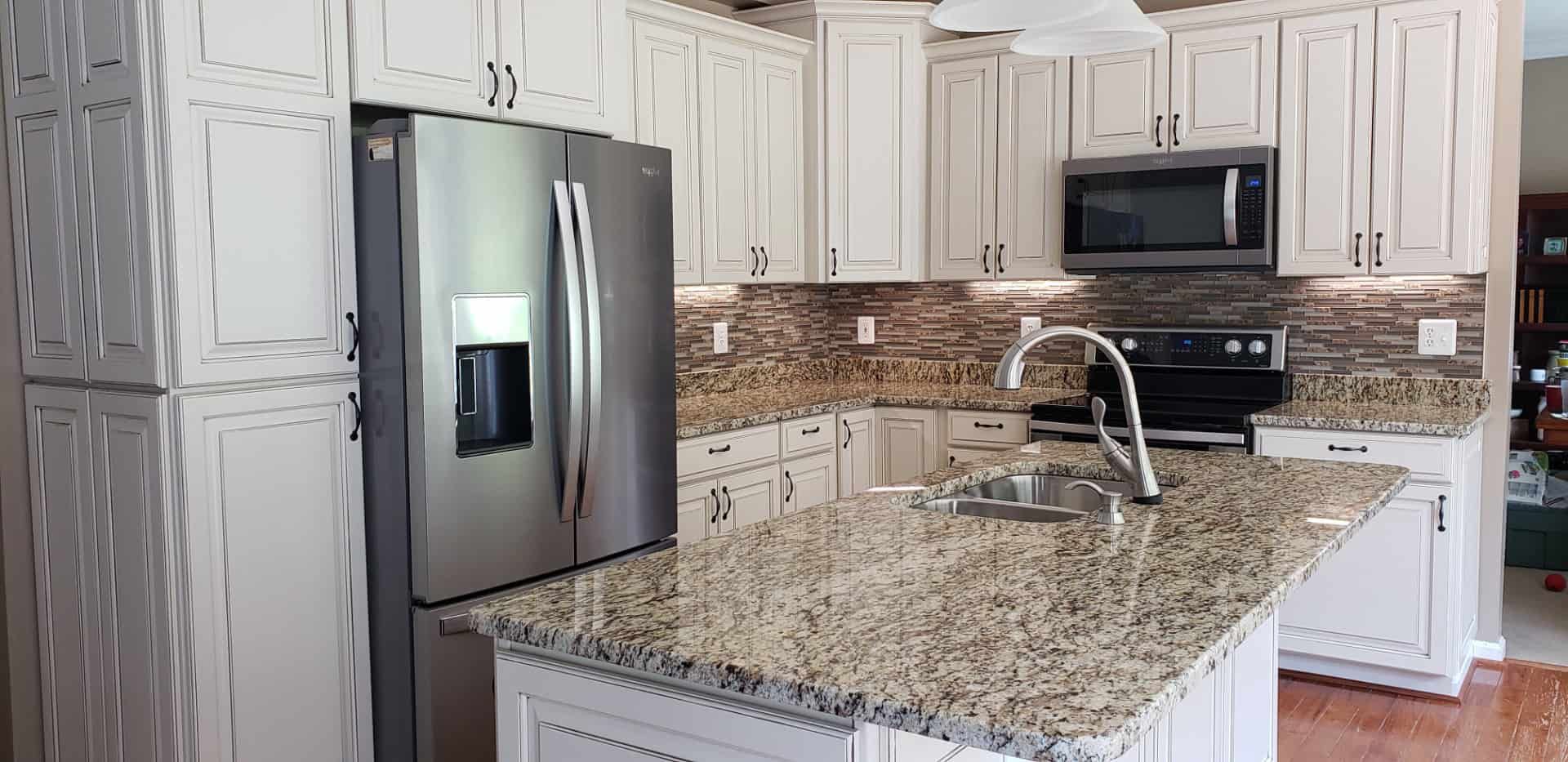 A kitchen with granite counter tops , white cabinets , stainless steel appliances and a refrigerator.