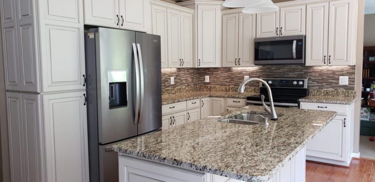 A kitchen with white cabinets , granite counter tops , stainless steel appliances and a refrigerator.