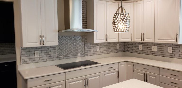 A kitchen with white cabinets , white counter tops , and a stove top oven.