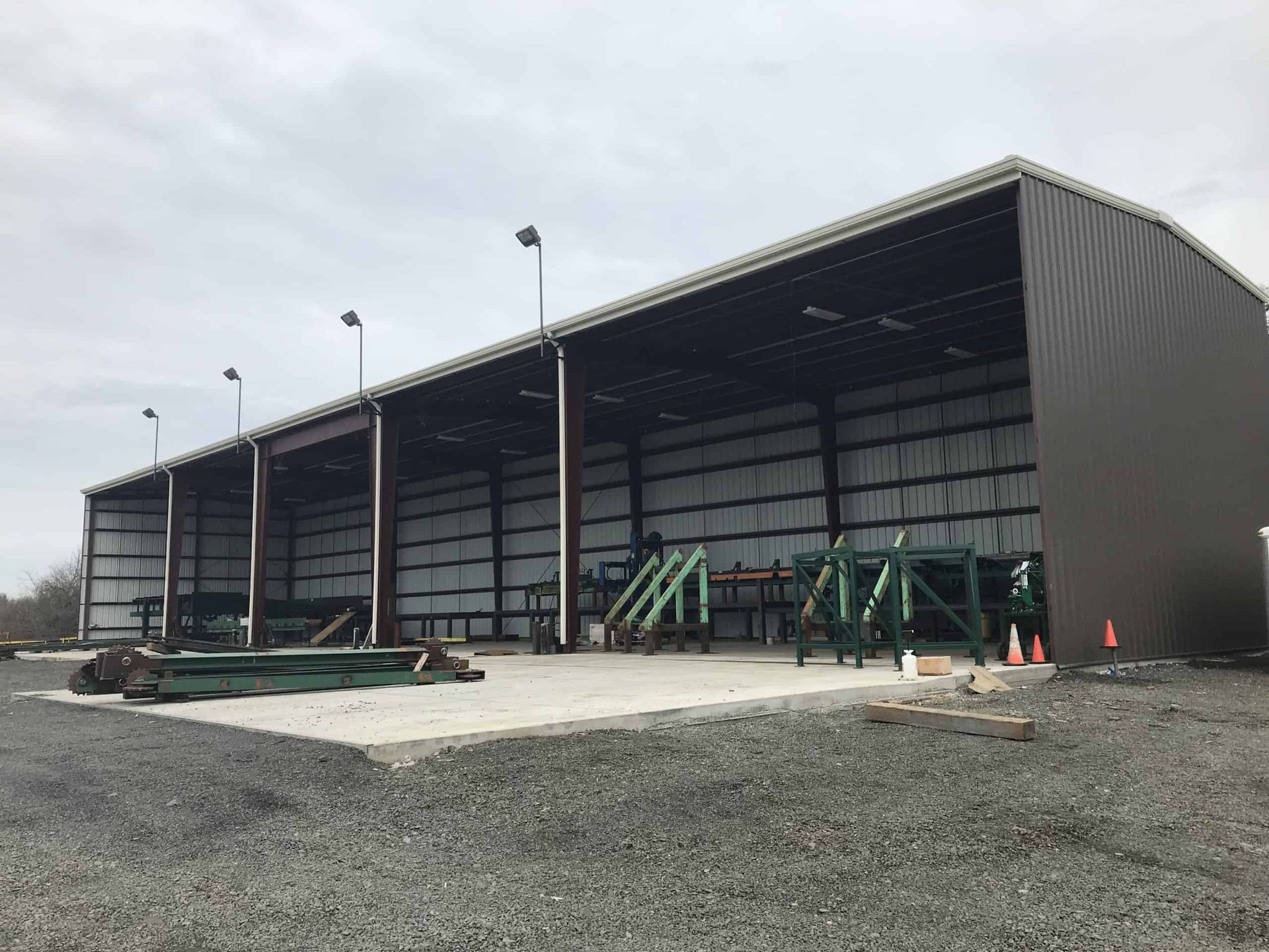 A large metal building with a roof is sitting on top of a gravel lot.