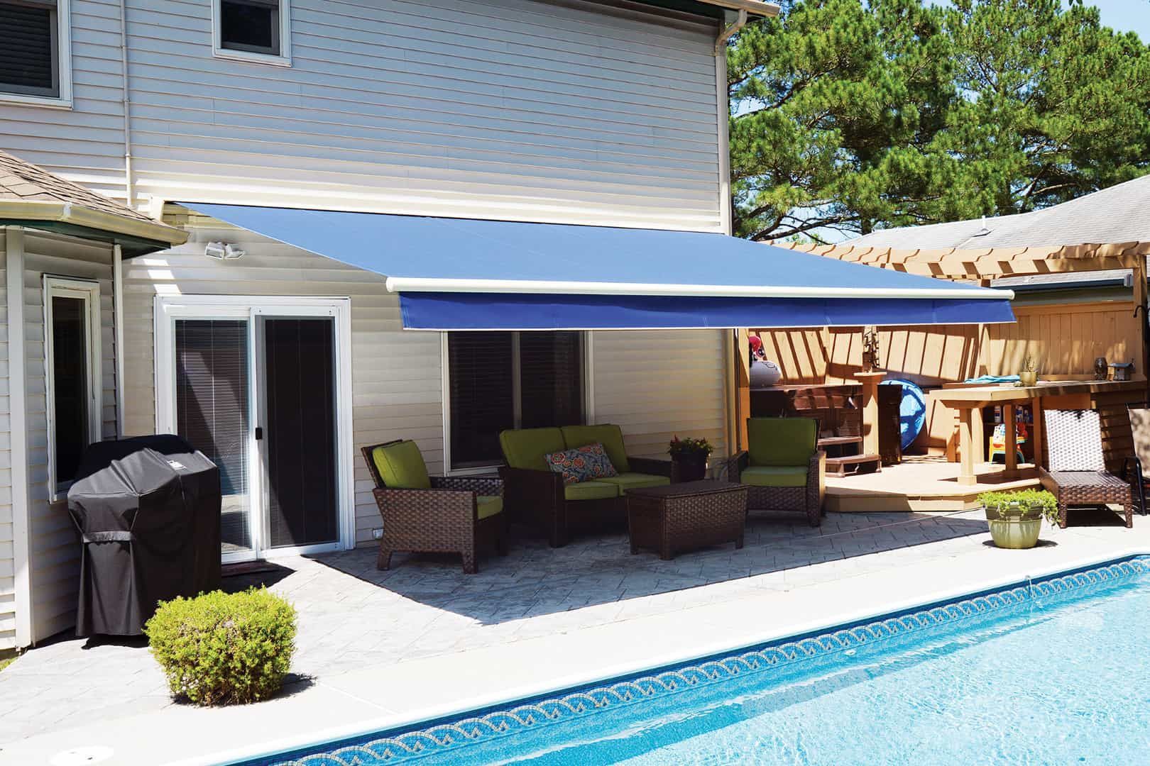 A patio with a blue awning over a swimming pool.