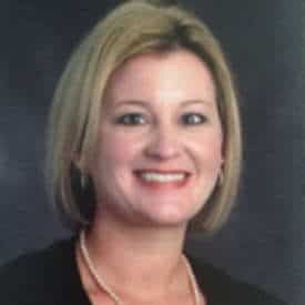 A woman wearing a black jacket and a necklace is smiling for the camera.