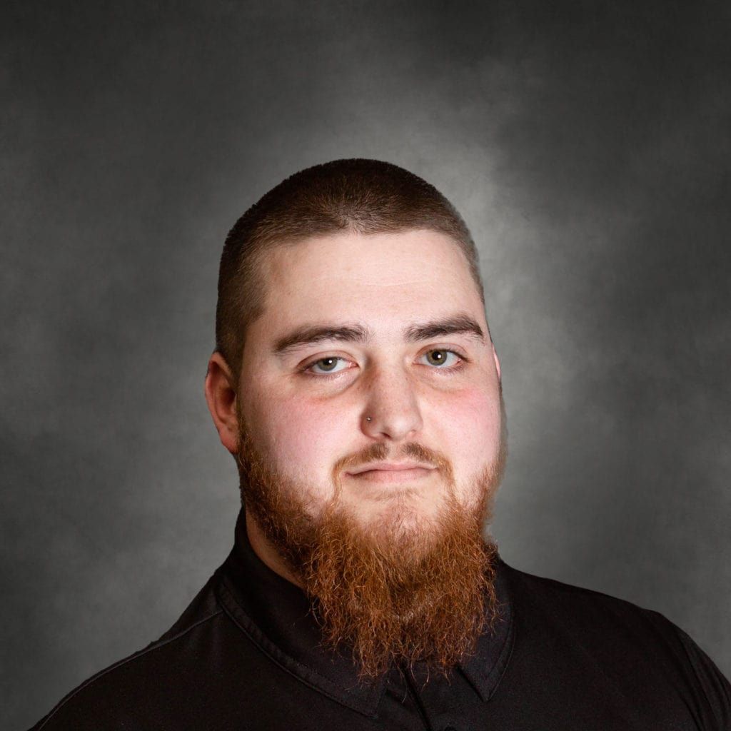 A man with a beard is wearing a black shirt and looking at the camera.