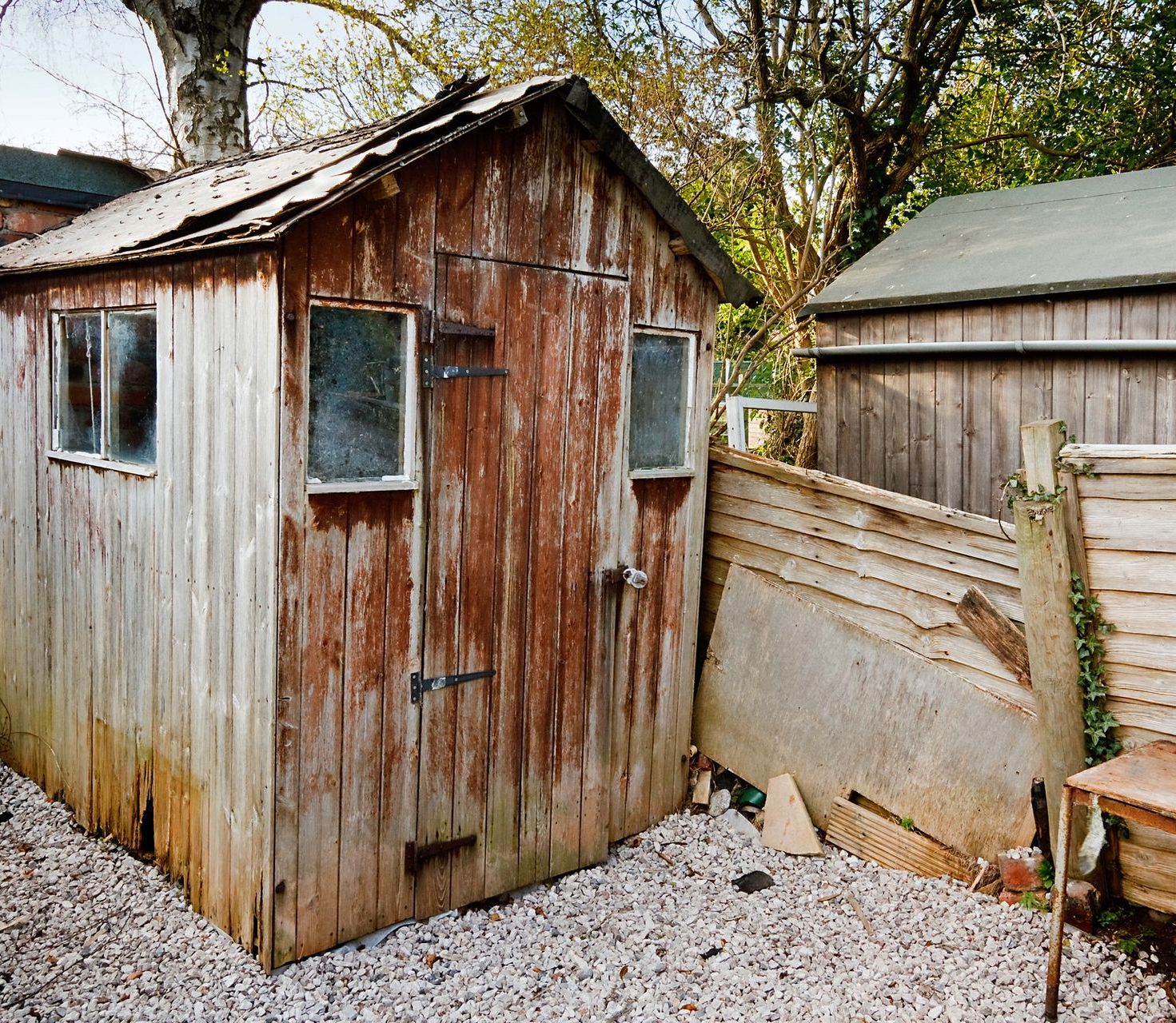 A wooden shed with a fence and gravel in front of it