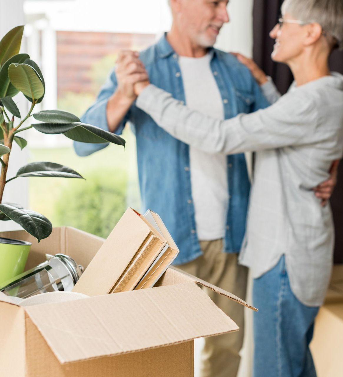 A man and woman are dancing in front of a cardboard box filled with books.