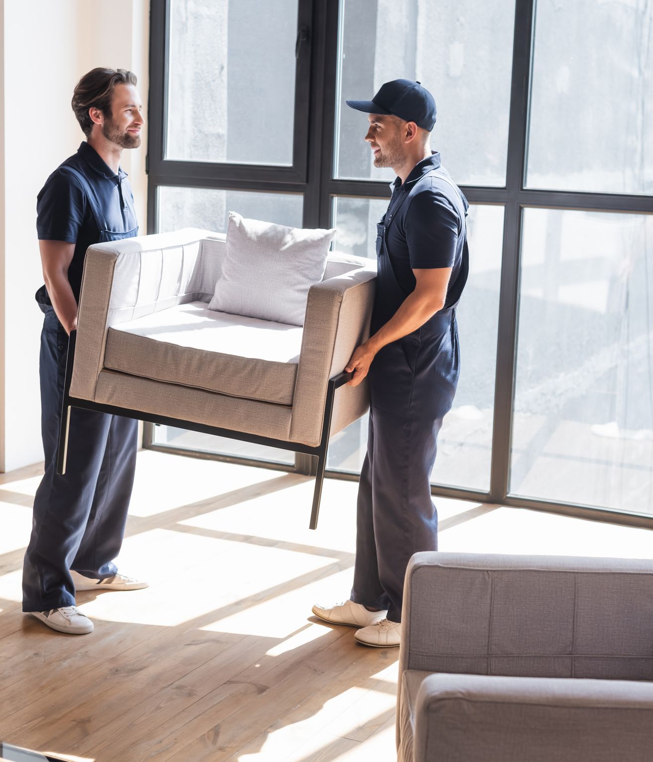 Two men are carrying a chair in a living room.