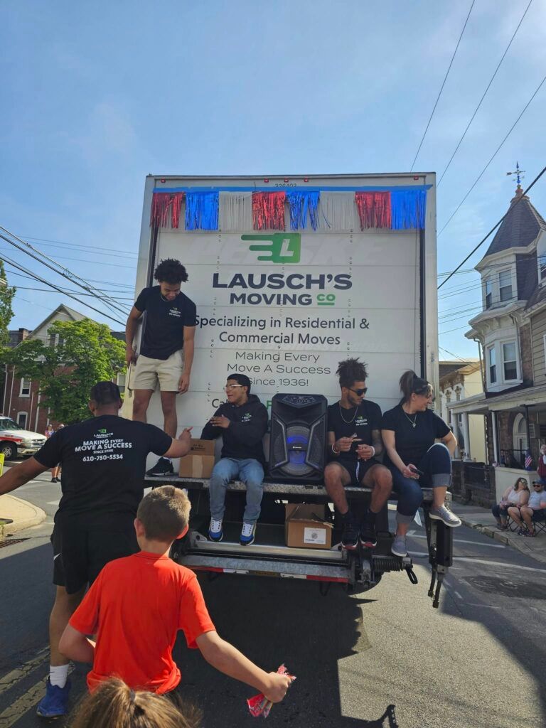Movers in blue uniforms loading cardboard boxes into a truck, outdoors.