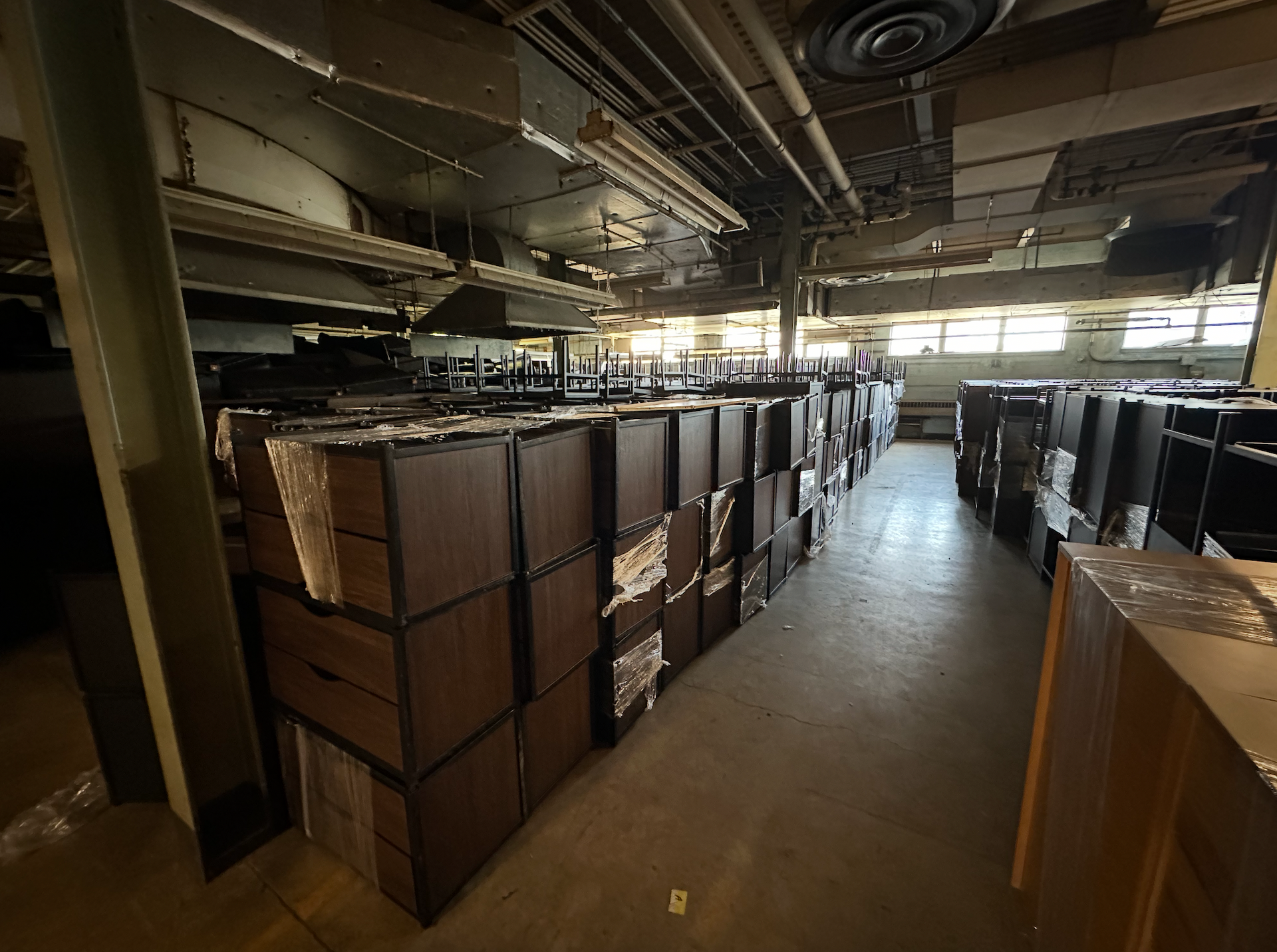 Three people carefully moving a piano, wrapped in plastic, in a room with hardwood floors.