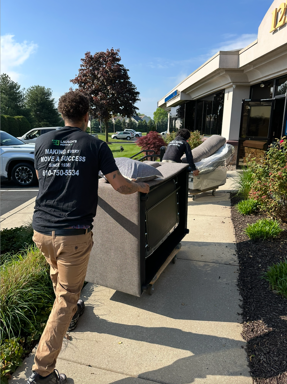 Movers in blue uniforms loading cardboard boxes into a truck, outdoors.