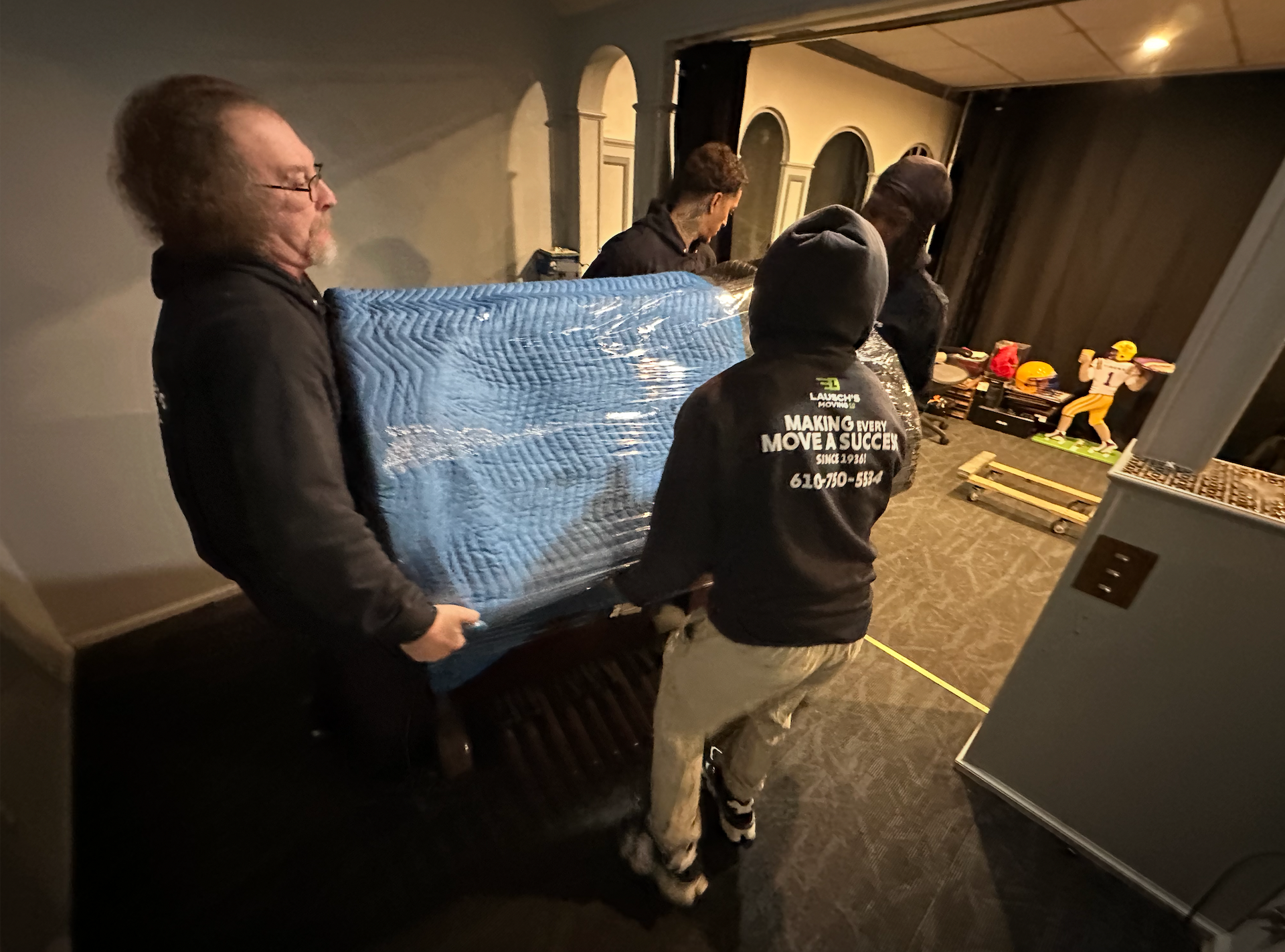 Movers in blue uniforms loading cardboard boxes into a truck, outdoors.