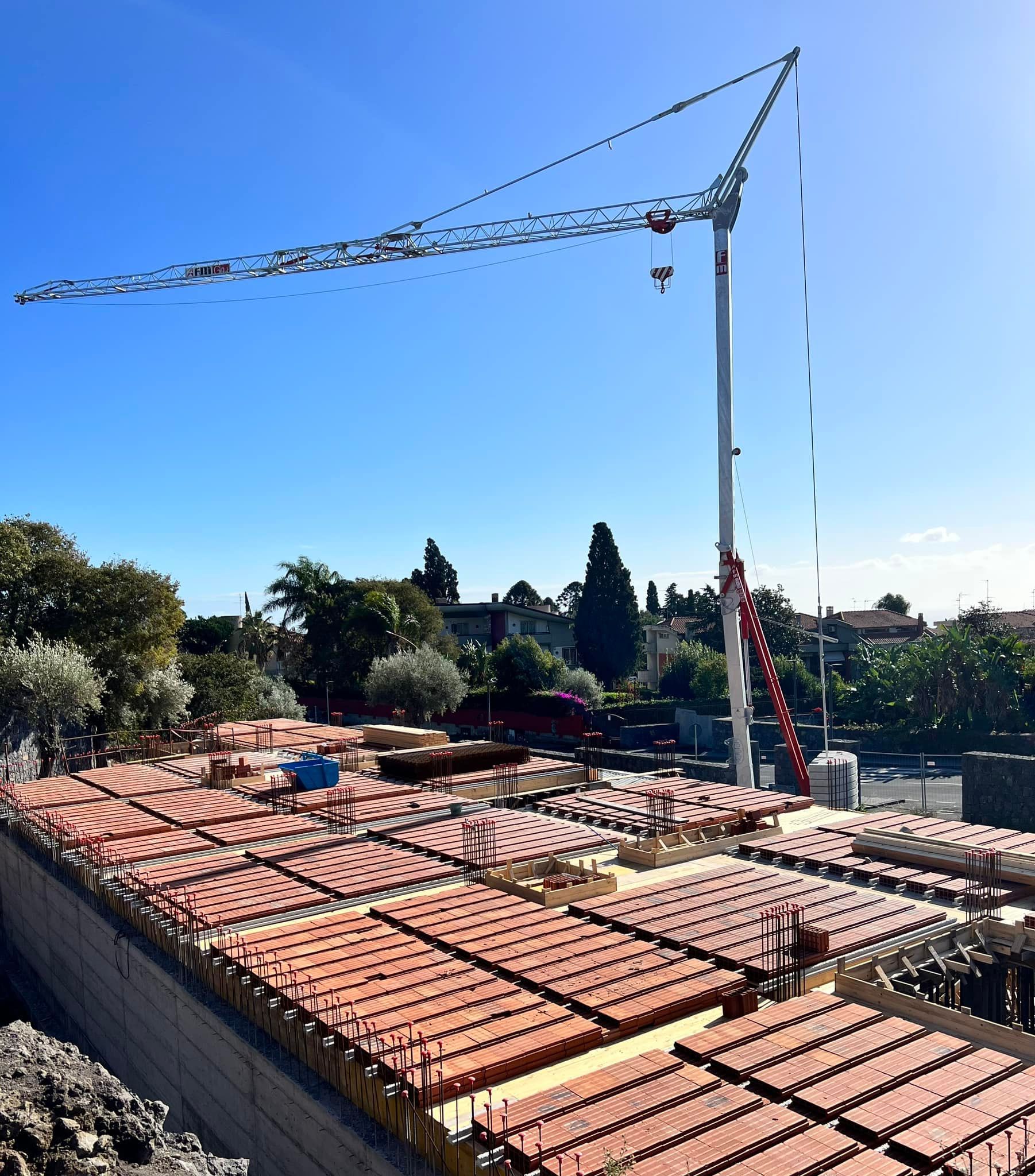 Cantiere con una gru alta sopra le tegole rosse in una giornata di sole.