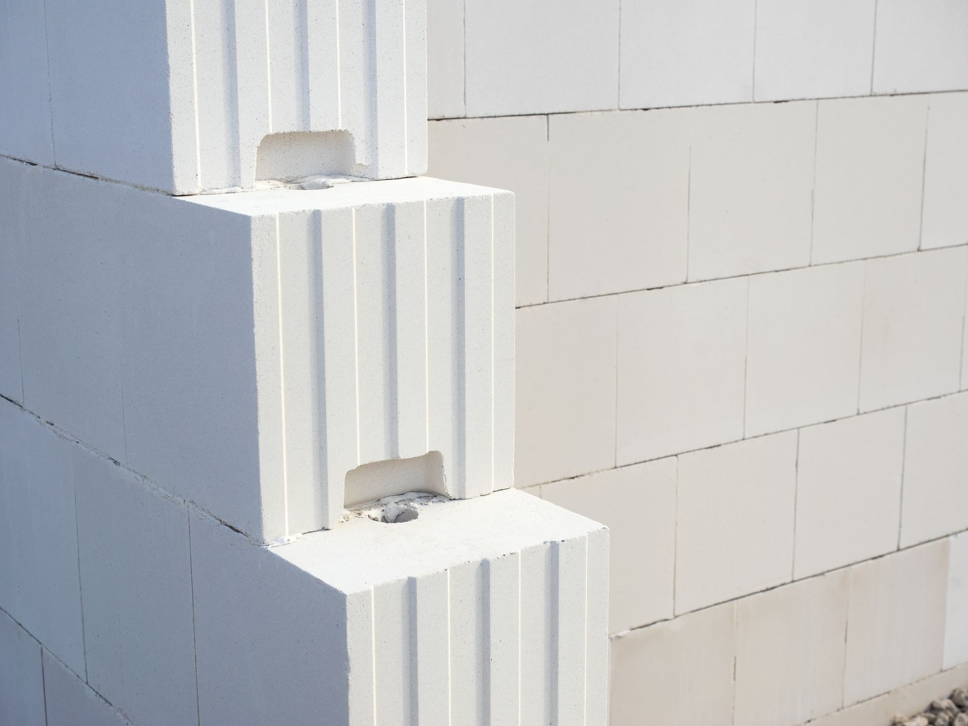 Weiße Bausteine, die zu einer Mauer gestapelt sind, mit vertikalen Rillen und rechteckigen Öffnungen.