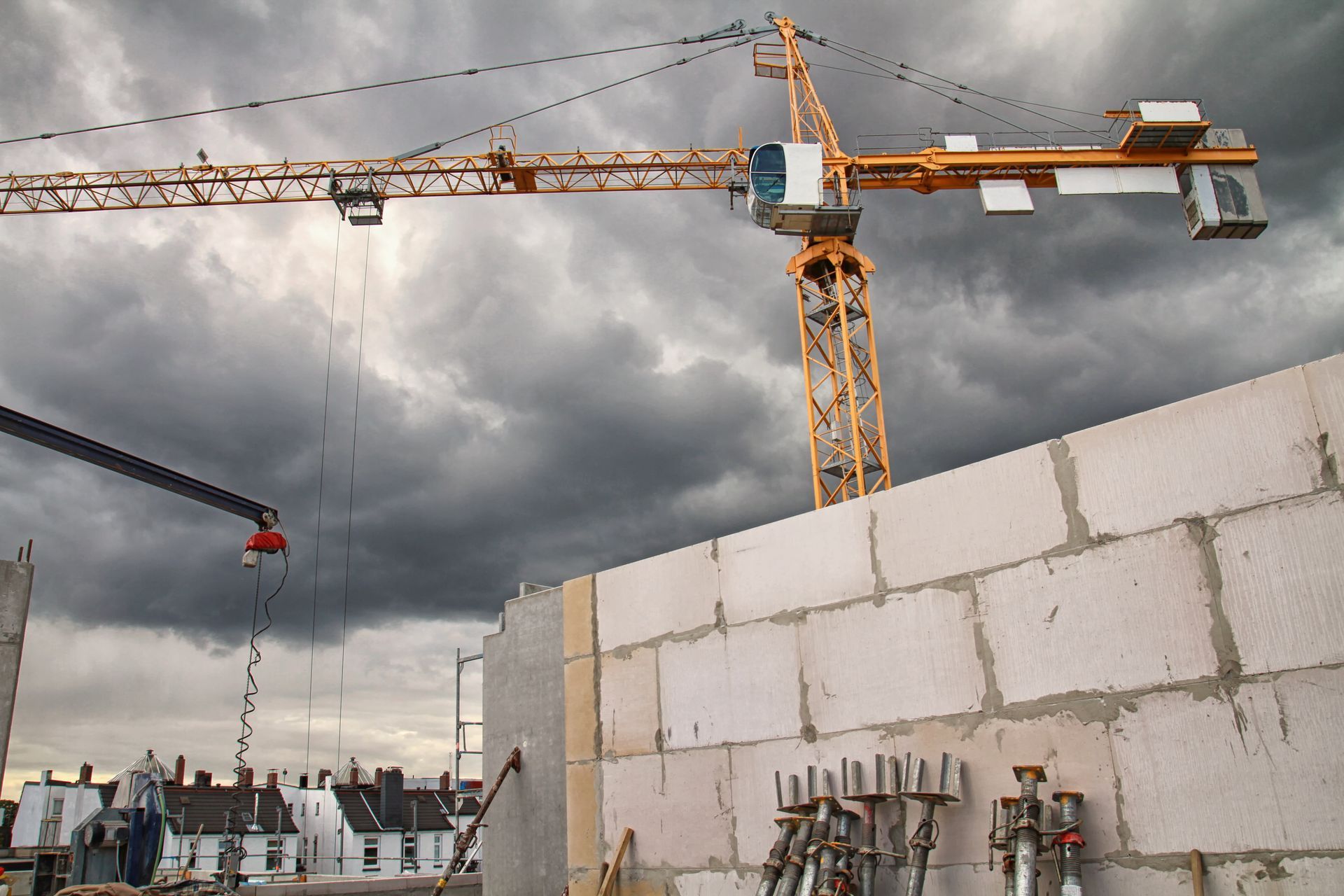 Baustelle mit einem gelben Kran, der unter einem stürmischen Himmel eine Ziegelmauer baut.