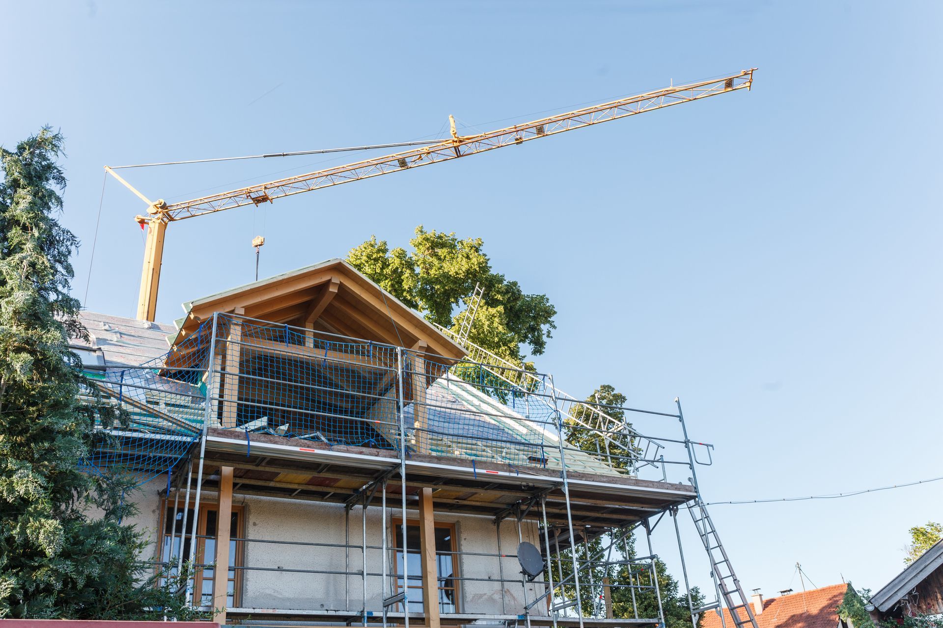 Bau eines Hauses mit Kran, Gerüst und teilweise fertigem Dach unter blauem Himmel.
