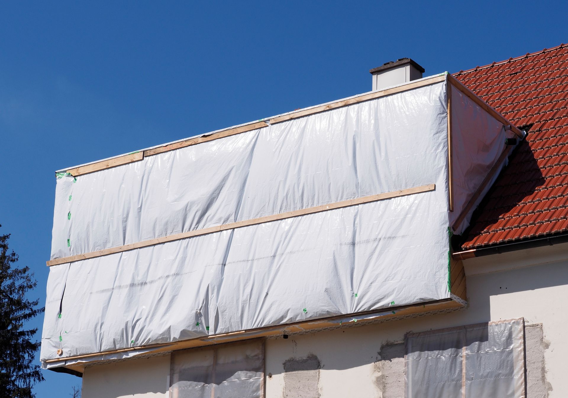 Ein mit Plastikfolie abgedeckter Dachabschnitt während Reparaturarbeiten an einem Gebäude.