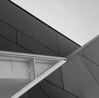 Geometrisches Architekturdetail in Graustufen: abgewinkelte graue und weiße Paneele, Fensterrahmen.