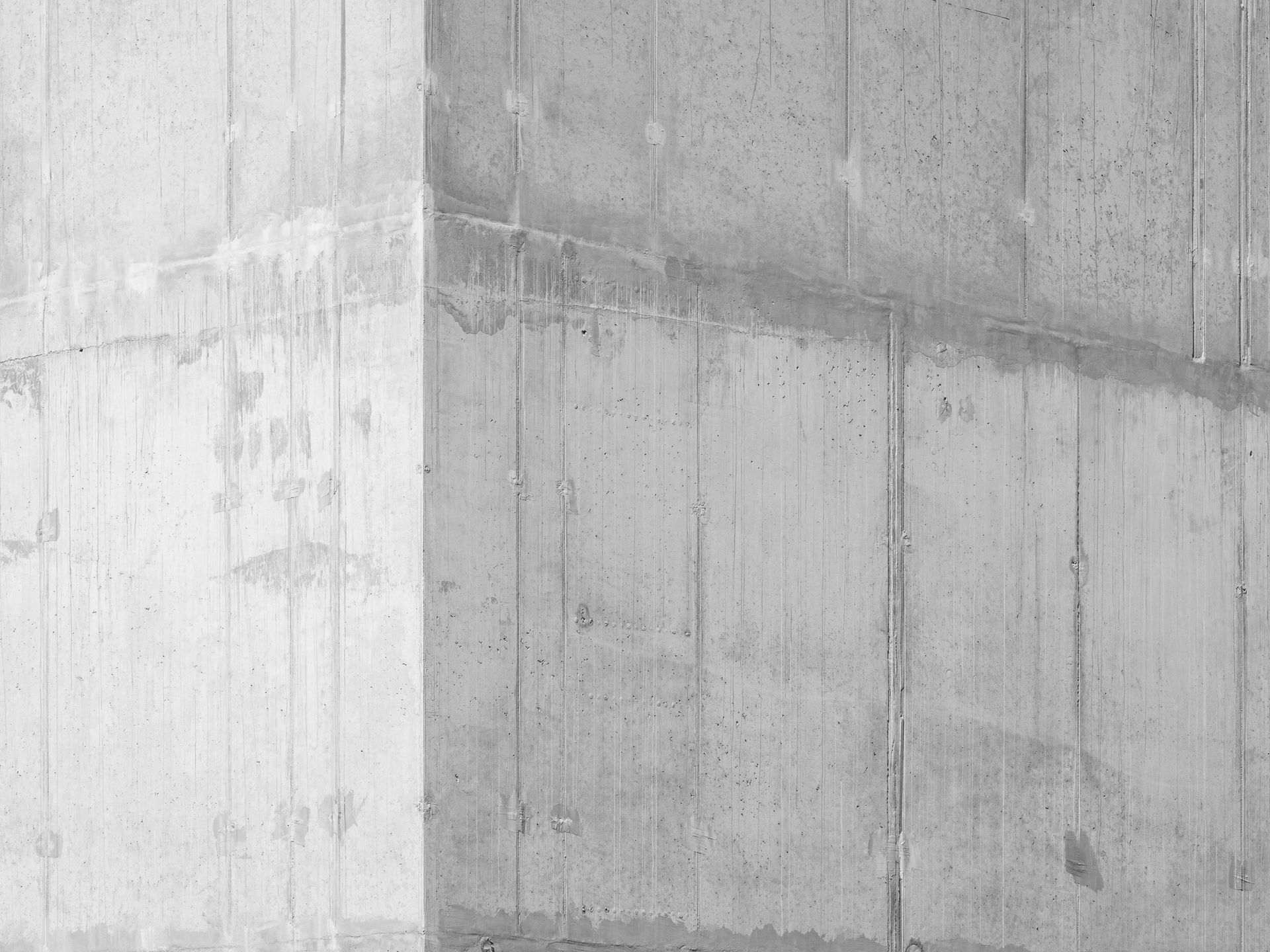 Graue Betonwand mit vertikalen Linien und Schatten.