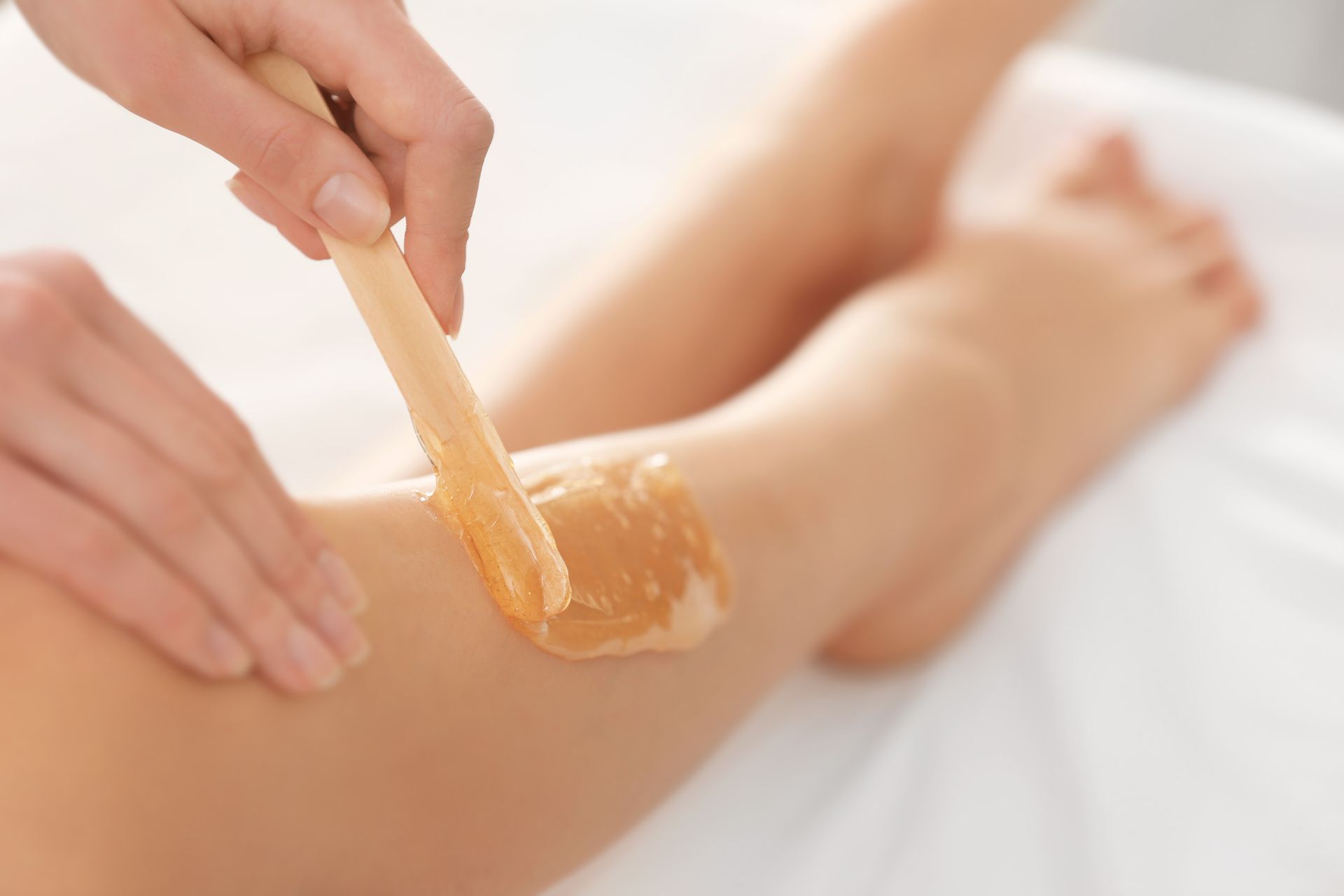 Wax being applied to a person's leg with a wooden spatula in a bright spa setting