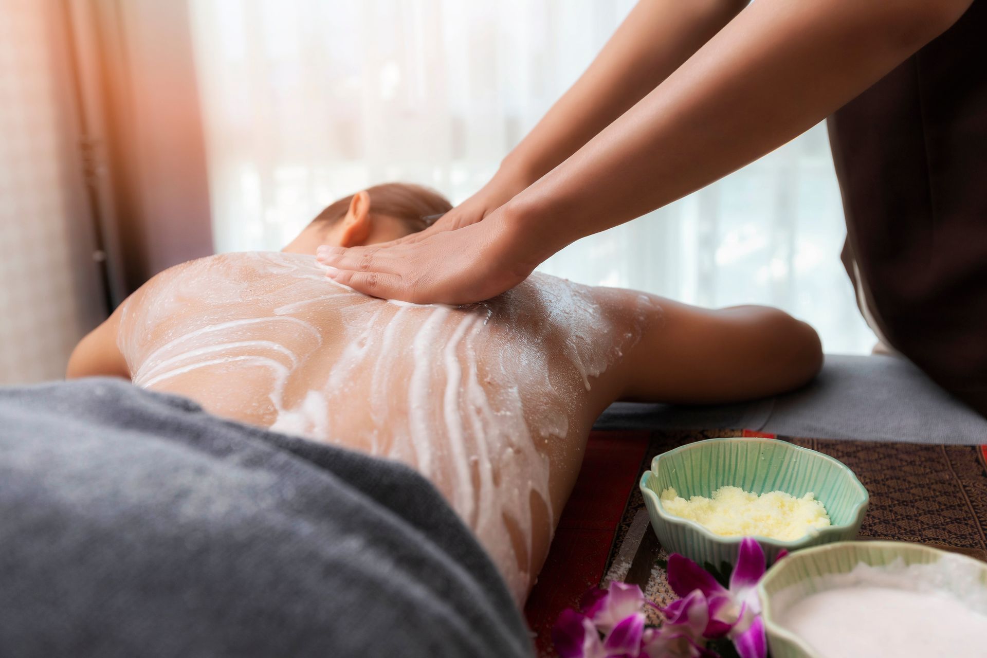 Massage therapist applying lotion to a client’s back on a spa table