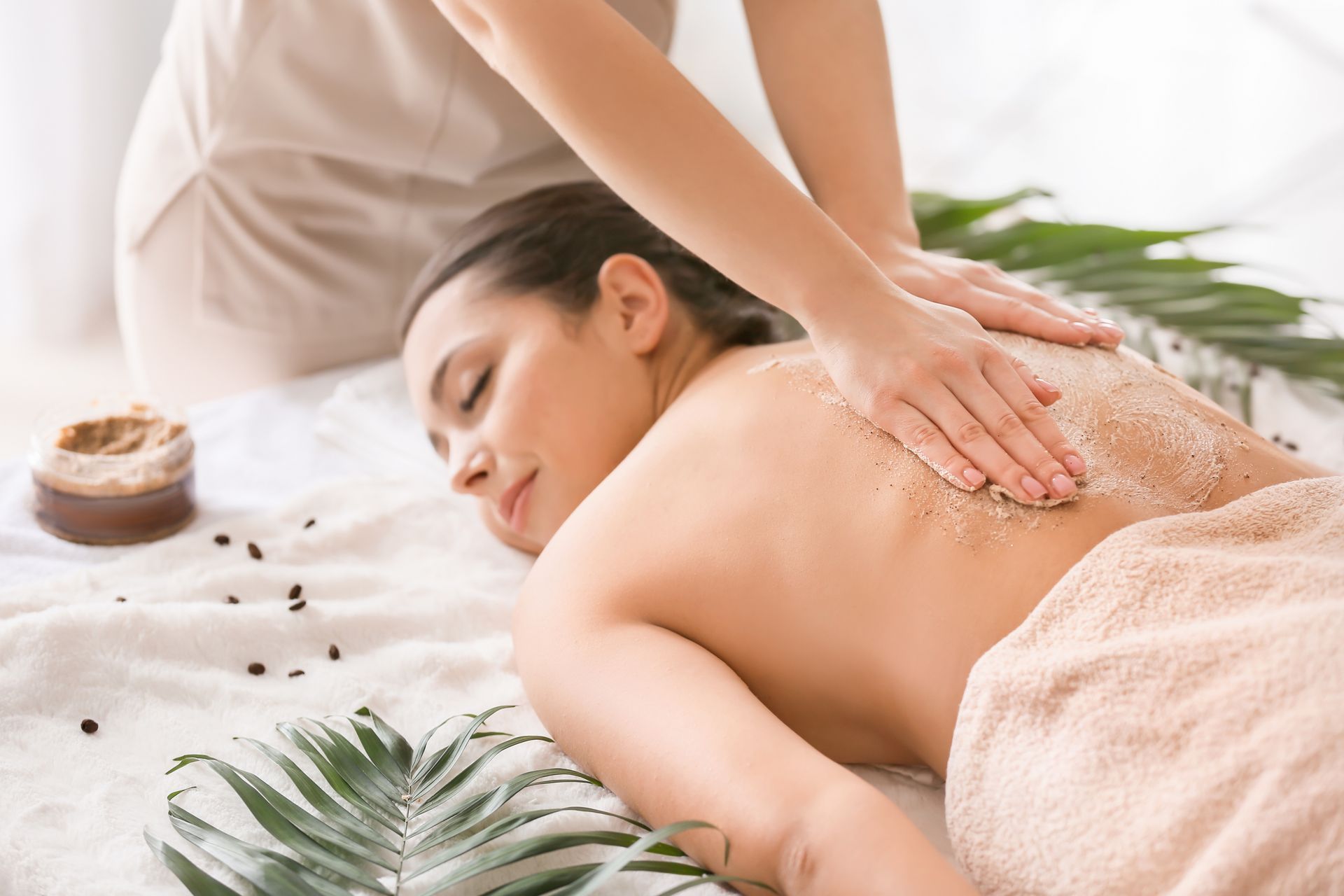 Woman receiving a back massage on a spa table, with green leaves and warm towels nearby