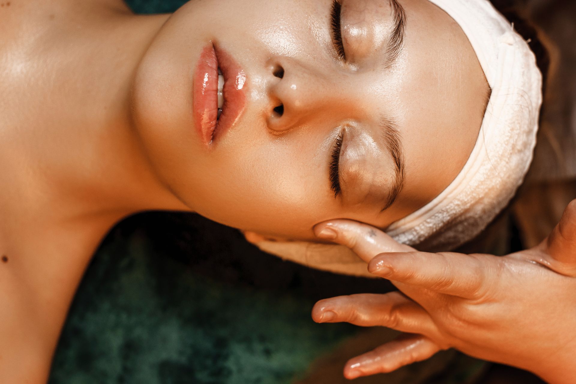 Woman receiving a spa facial massage with a white headband and closed eyes