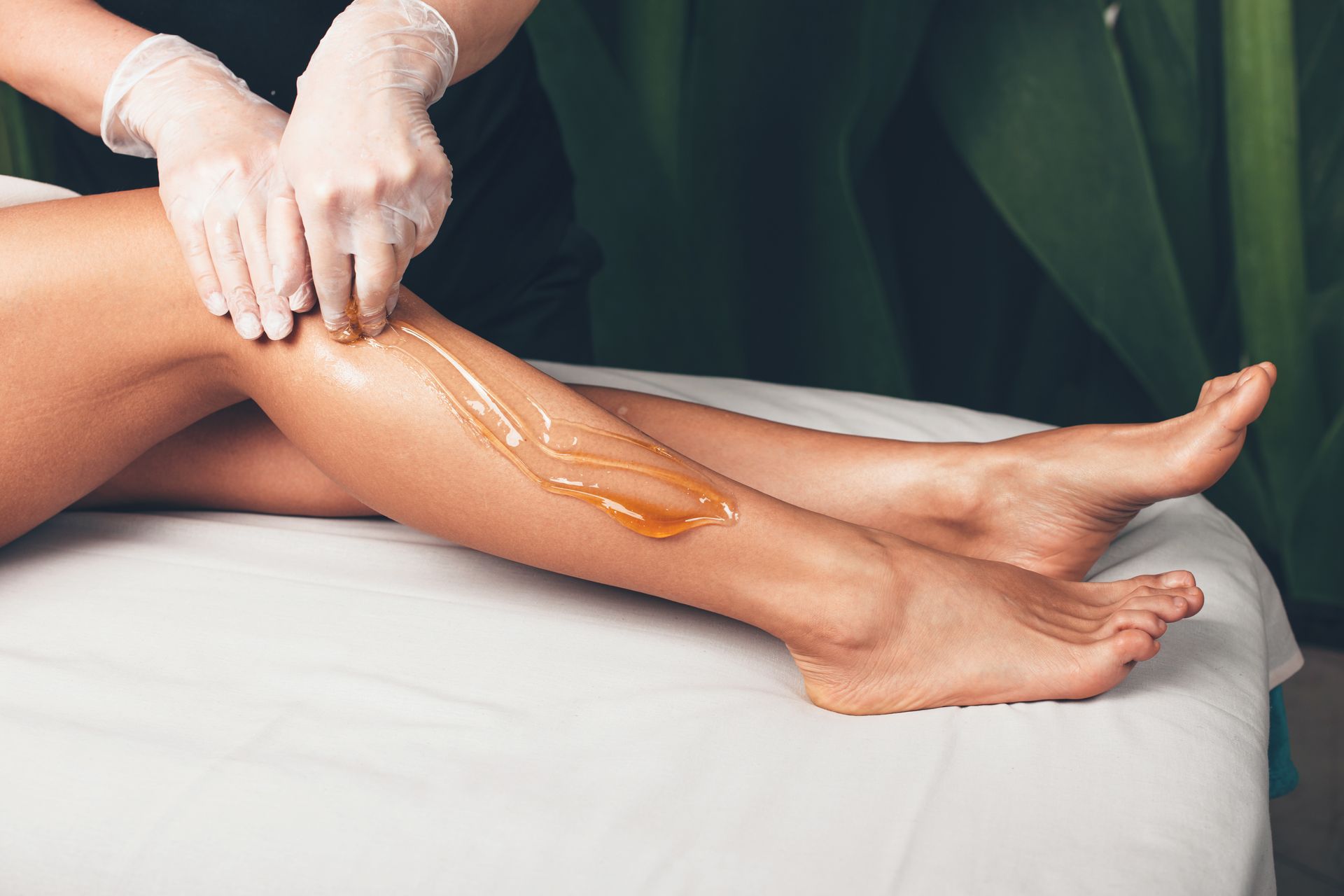 Hands applying wax to a client’s leg on a spa treatment table