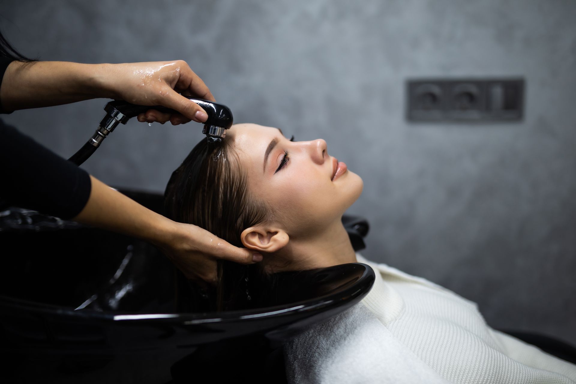 Person reclining at a salon sink while having hair washed by a stylist