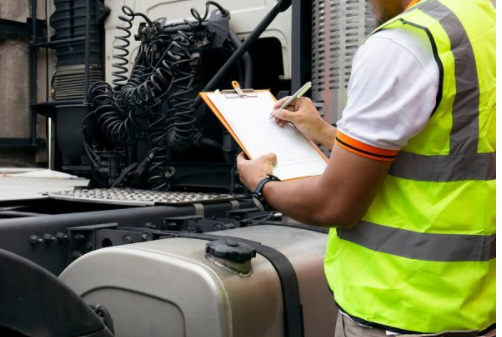 A man in a yellow vest is writing on a clipboard in front of a truck.